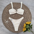 White bikini set with bow design on a woven mat with flowers and starfish.
