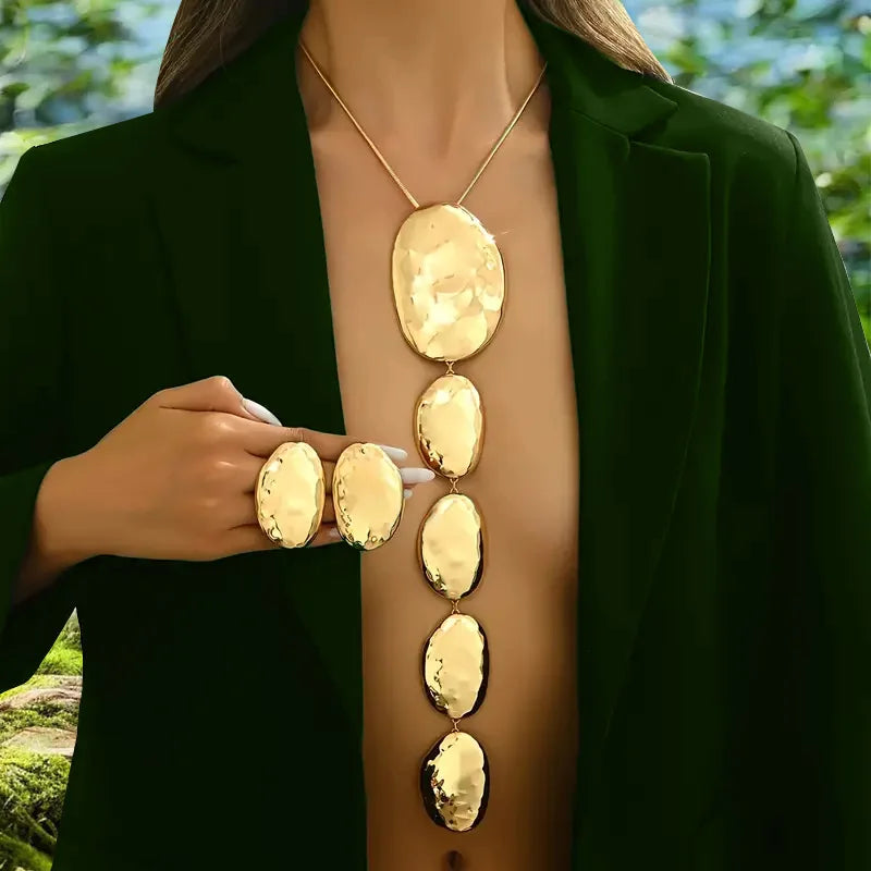 Gold necklace and rings on a mannequin with a green jacket against a blurred natural background
