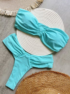 Turquoise two-piece swimsuit on a textured surface with woven mats.