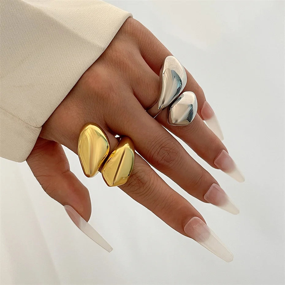 Hand wearing gold and silver rings with long, pointed nails on a neutral background