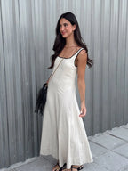 Woman in a white dress standing against a gray corrugated metal wall.