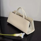 White handbag on a black surface with a white flower beside it
