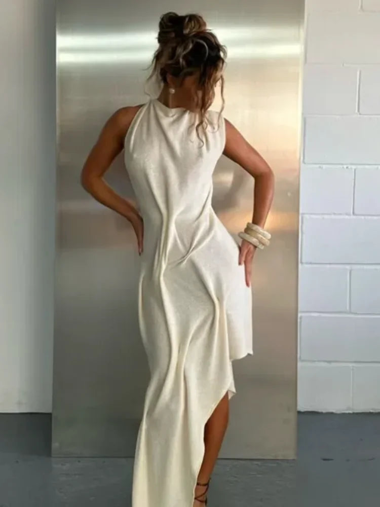 Woman wearing a white sleeveless dress with a high slit, standing against a plain wall.