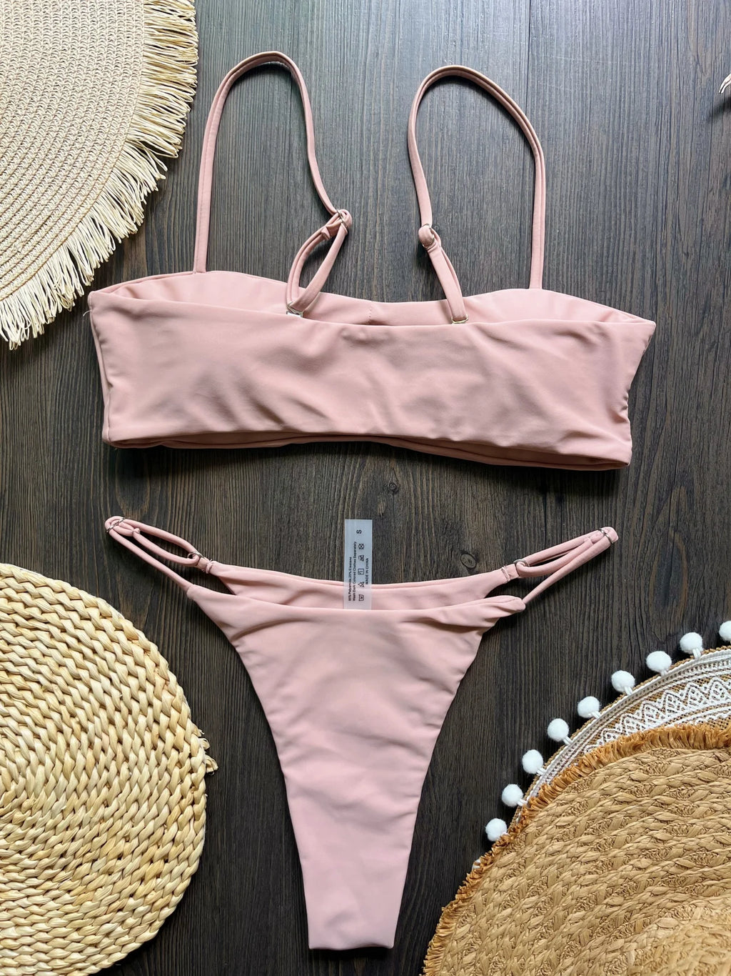 Pink bikini set on a dark wooden surface with decorative mats.