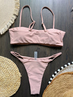 Pink bikini set on a dark wooden surface with decorative mats.