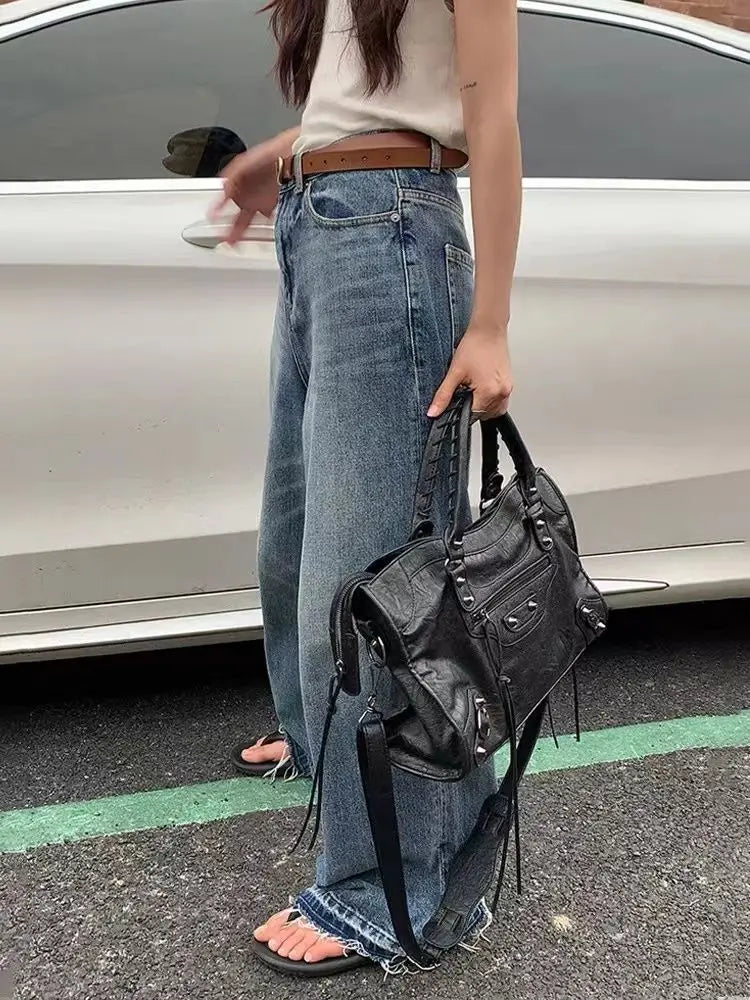Person wearing blue jeans and a black leather bag, standing next to a car.
