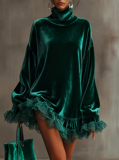 A woman models an oversized emerald green velvet turtleneck top with dramatic ruffled lace trim at the hem and cuffs, styled with a matching green handbag against a textured gray studio background.