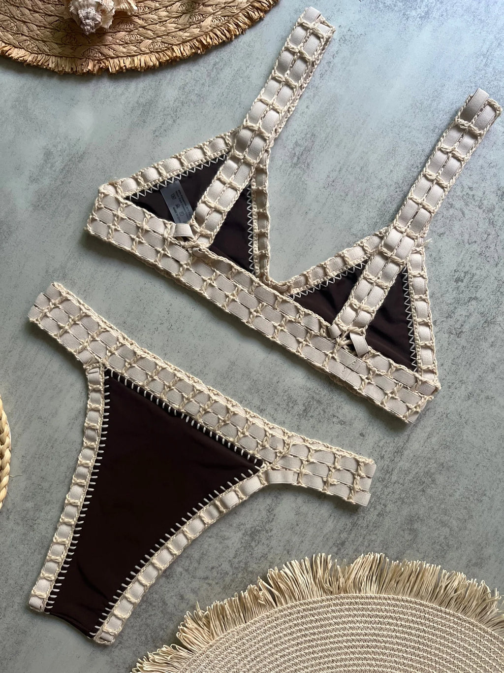 Beige and black bikini set on a textured surface with straw hats.
