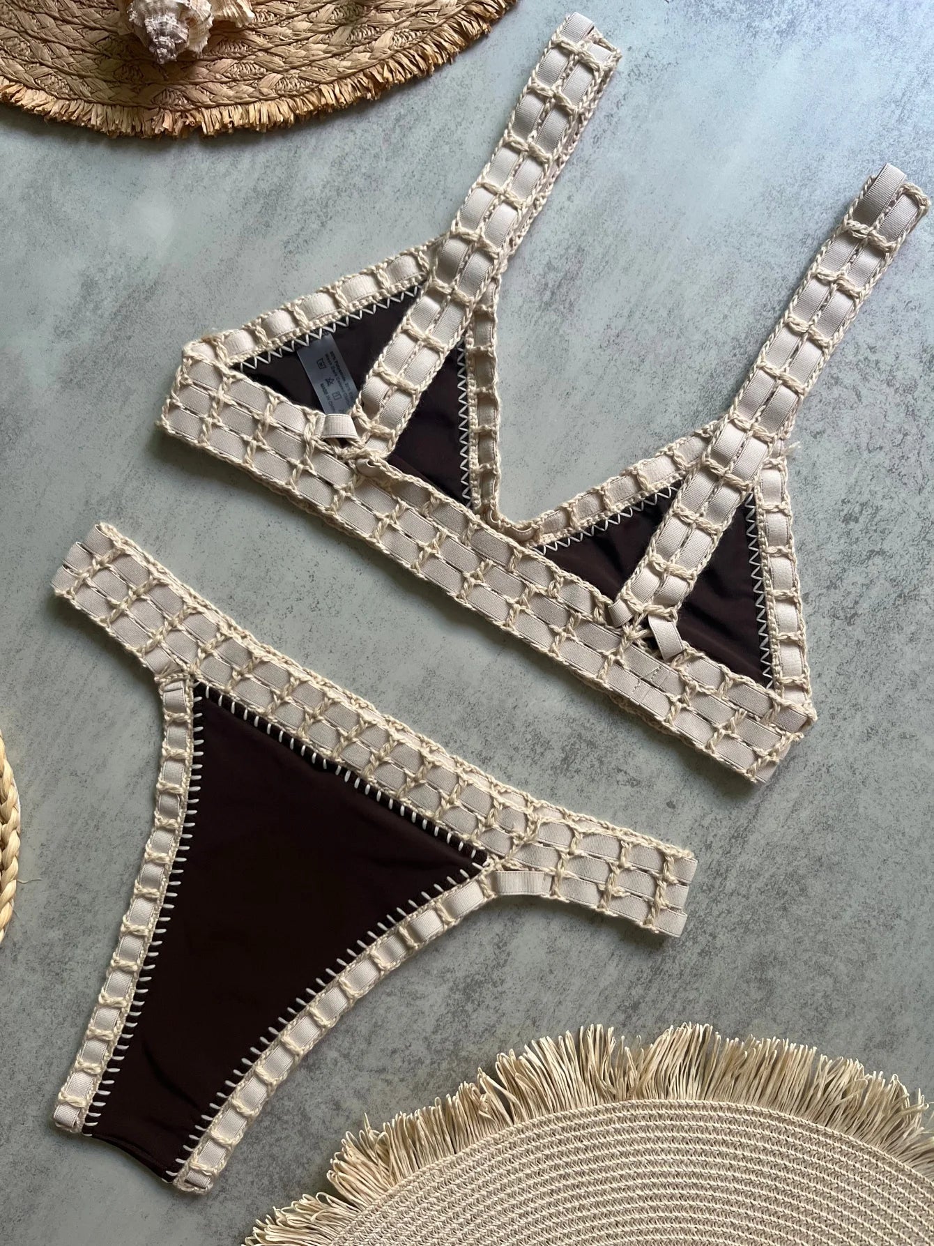 Beige and black bikini set on a textured surface with straw hats.