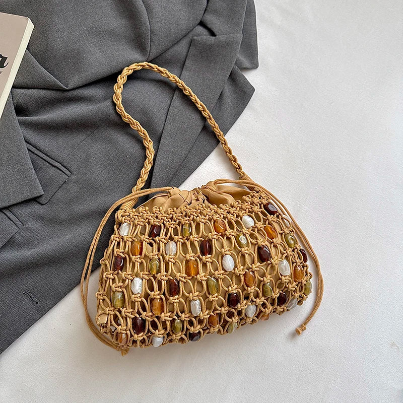 A woven straw handbag with a braided shoulder strap, decorated with colorful faux-amber and white stone accents, styled on a white surface next to a gray blazer.