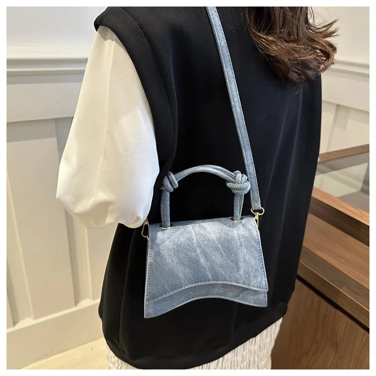 Person wearing a black vest over a white shirt with a denim handbag.