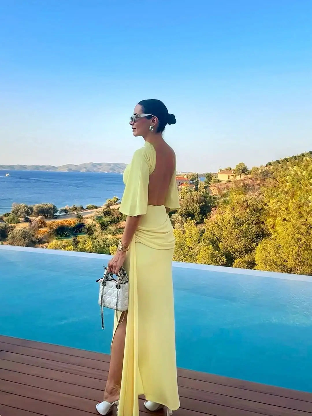 Woman in a yellow dress standing by an infinity pool with a scenic view.