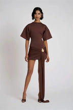 Woman wearing a brown outfit with a draped skirt on a white background