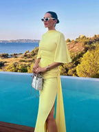 Woman in a yellow dress standing by a pool with a scenic background