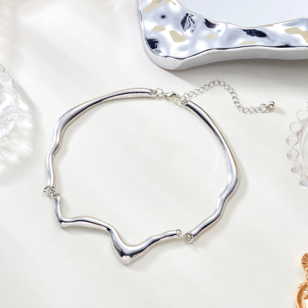Silver necklace on a white surface with a textured silver object in the background