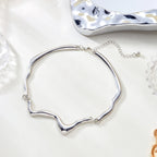 Silver necklace on a white surface with a textured silver object in the background