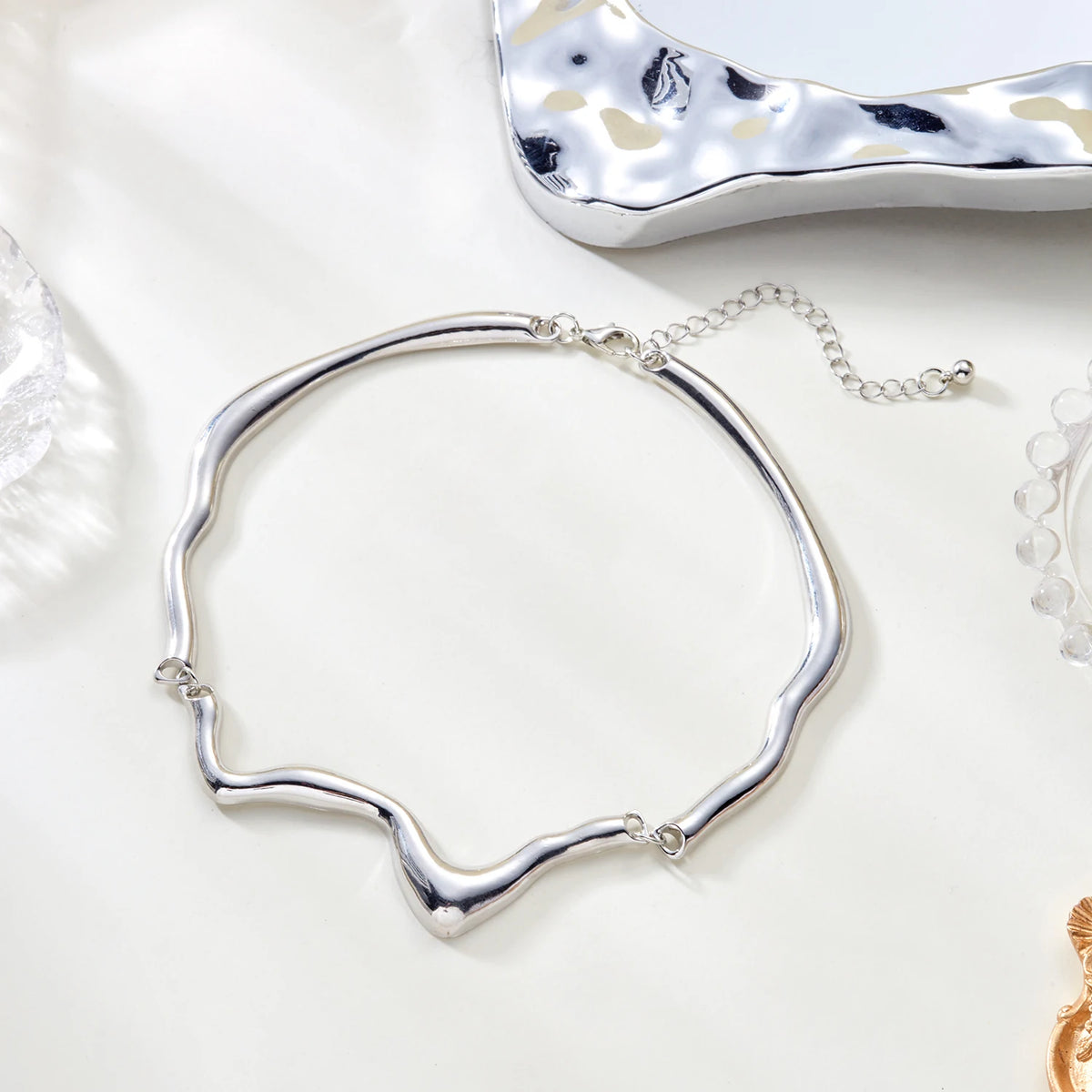 Silver necklace on a white surface with a textured silver object in the background
