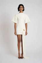 Woman wearing a white dress with a slit on a plain background