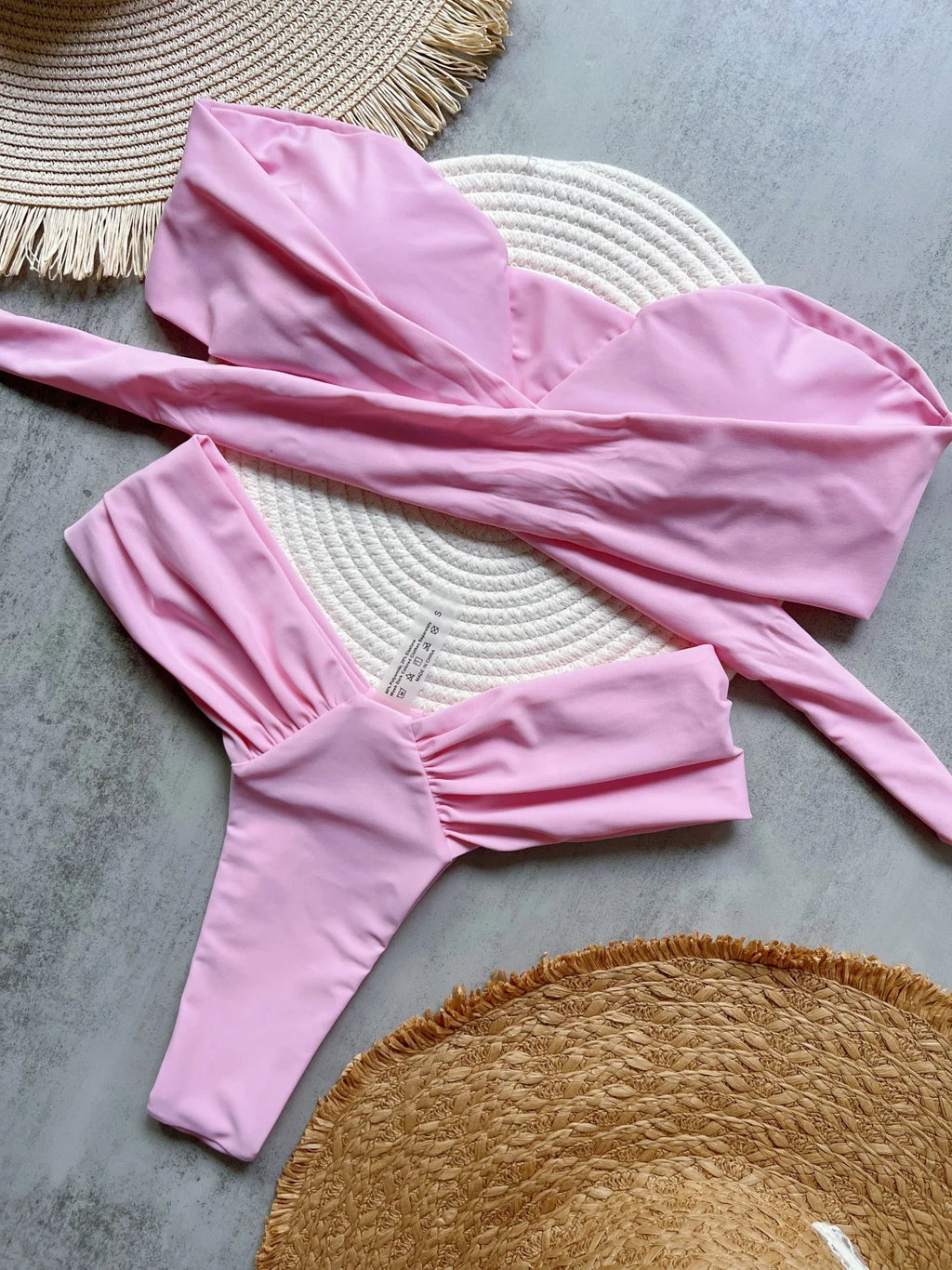 Pink swimsuit laid out on a textured surface with woven mats.
