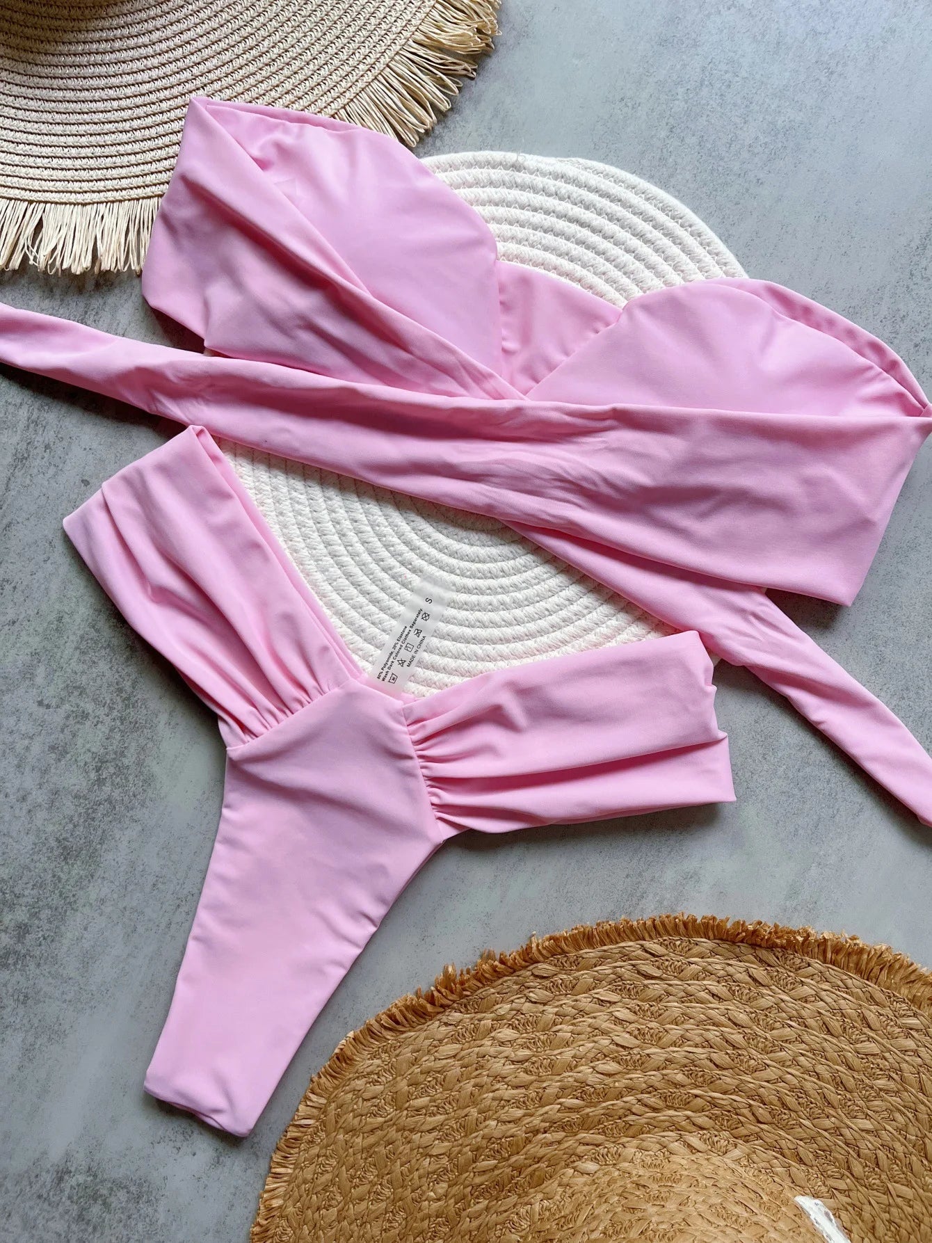 Pink swimsuit laid out on a textured surface with woven mats.