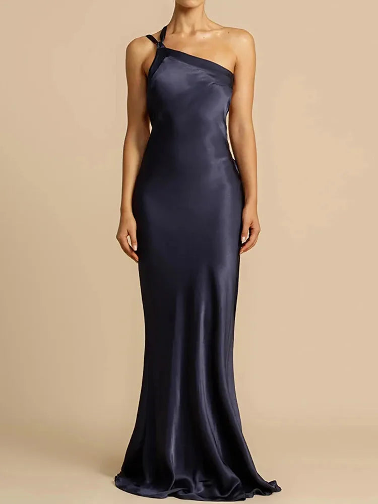 A woman wearing a red, solid color, diagonal collar, spaghetti strap, maxi dress that reaches the floor.