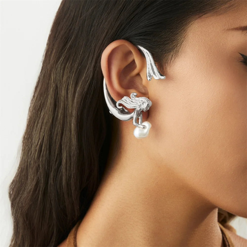 Close-up of a woman wearing silver ear cuffs with a pearl drop on a plain background