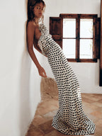 Woman wearing a black and white polka dot dress standing in a room with a wooden window.