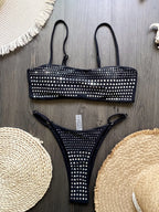 Black studded bikini set on a wooden surface with woven coasters.