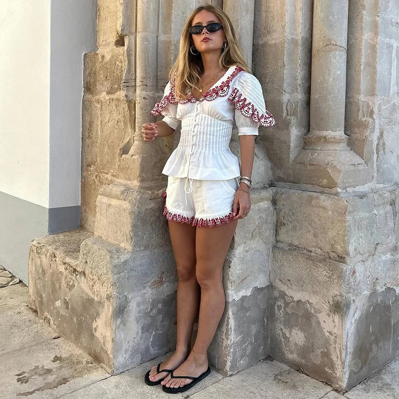 Woman in a white outfit with red details leaning against stone columns.