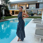 Woman in a dark blue dress standing by a pool with a modern house in the background