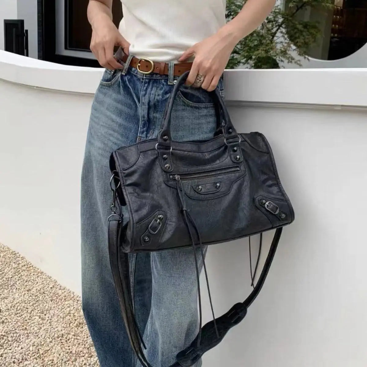 Person holding a black leather handbag with a white background