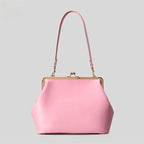 A light pink leather handbag with a gold-tone kiss-lock frame and a matching pink shoulder strap, shown against a solid light gray background.