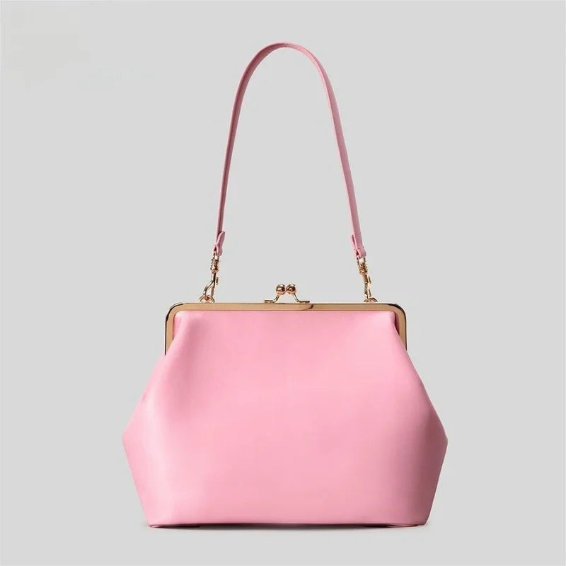A light pink leather handbag with a gold-tone kiss-lock frame and a matching pink shoulder strap, shown against a solid light gray background.
