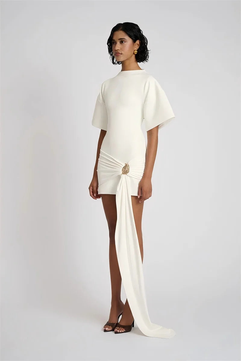 Woman wearing a white dress with a draped design on a plain background