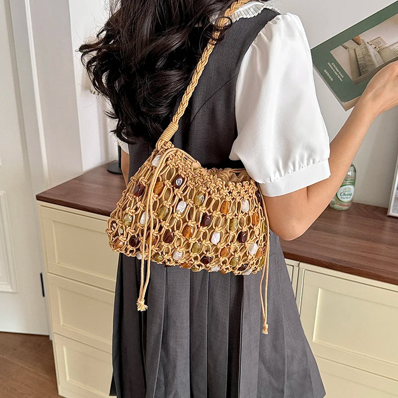 A woman wearing a dark gray dress with a white puff-sleeve shirt, carrying a tan woven shoulder bag with brown and amber stone accents in a home setting.