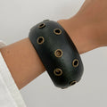 Black wristband with circular holes on a person's arm against a light background