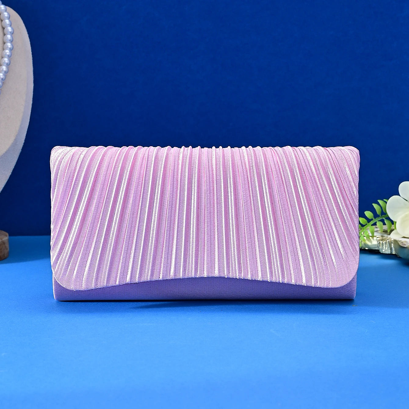 Pink pleated clutch bag on a blue surface with a blue background