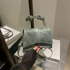 Green suede handbag with knotted handle held by a hand on a surface with books.