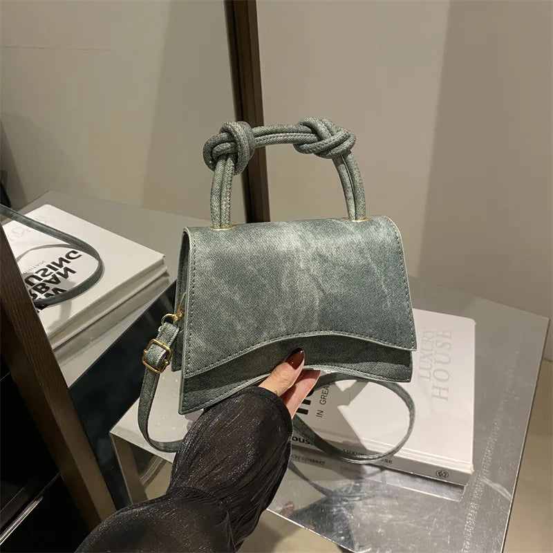Green suede handbag with knotted handle held by a hand on a surface with books.
