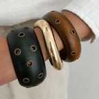 Three wooden bracelets in black, gold, and brown on a person's wrist against a light background.