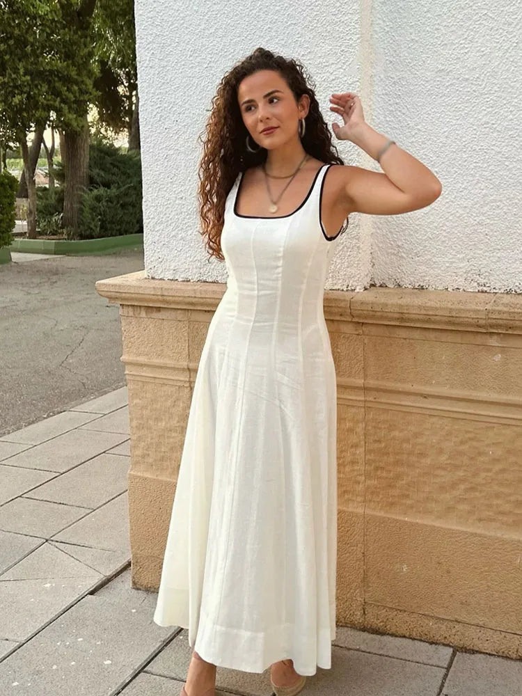 Woman in a white dress standing outdoors against a textured wall.