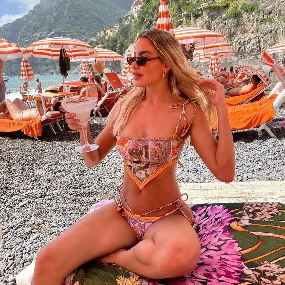 Woman in a colorful bikini sitting on a beach with umbrellas and lounge chairs.