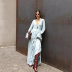 Woman in a light blue dress and red boots standing against a textured wall.