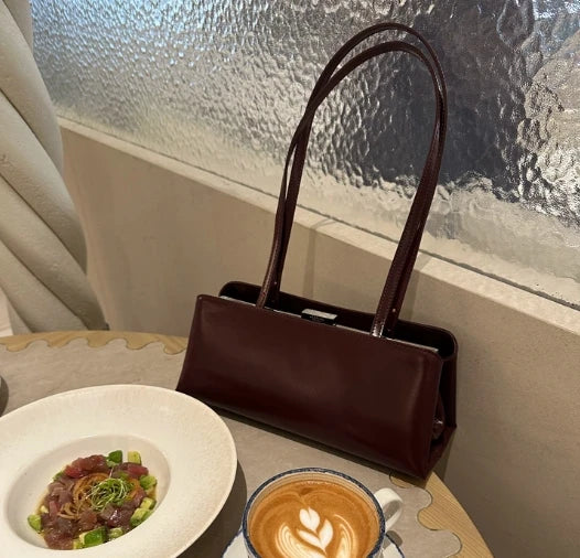 Brown leather handbag on a table with a dish and coffee cup.