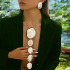 Woman wearing a long, elegant necklace with large, round, silver pendants against a natural background.