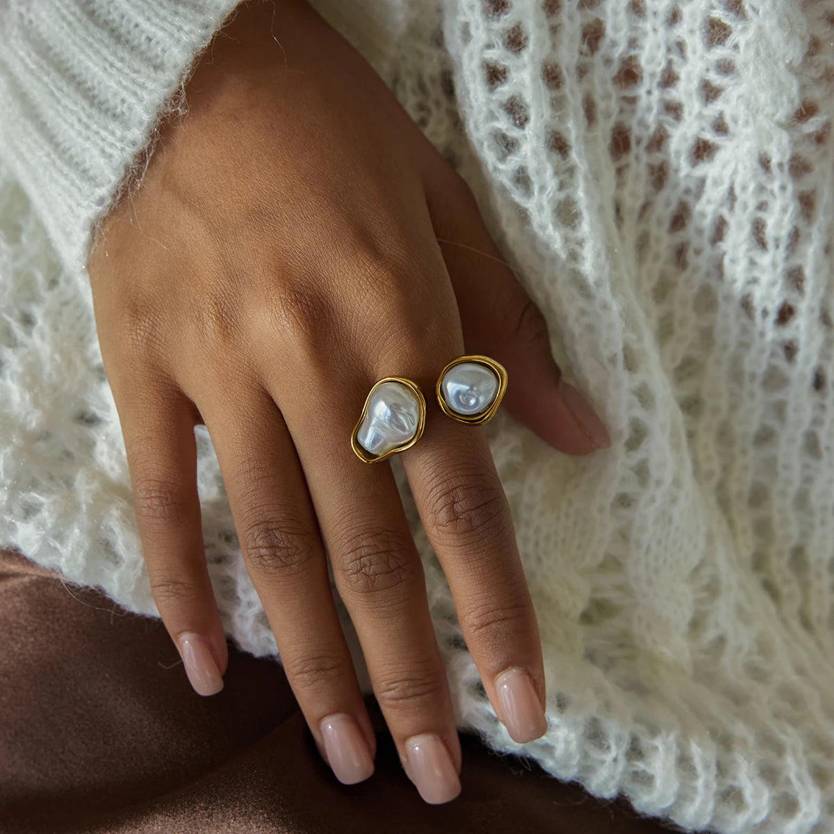 Hand wearing a gold ring with a heart-shaped pearl on a textured white fabric background