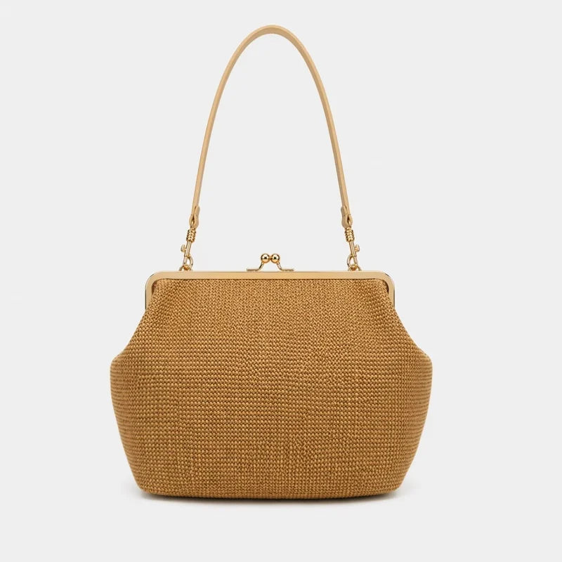 A structured woven straw handbag in a warm tan color, featuring a single shoulder strap, gold-tone metal frame, and a kiss-lock clasp, set against a plain light gray background.