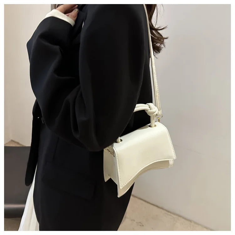 Person wearing a black coat holding a white handbag against a neutral background