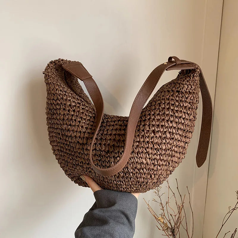 Brown woven handbag with leather straps held by a person against a neutral background