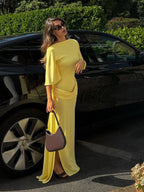 Woman in a yellow dress standing next to a black car outdoors.